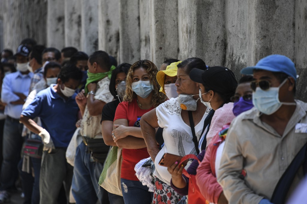 People wear face masks against the spread of the new coronavirus as they queue to enter a bank in San Salvador on March 30, 2020. - Thousands of Salvadorans in different parts of the country were desperately seeking to receive the aid of $300 from the government for the purchase of food Monday during the outbreak of the new coronavirus pandemic. (Photo by Yuri CORTEZ / AFP)